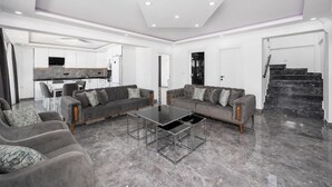 Ein modernes Wohnzimmer mit zwei grauen Sofas, einem Glastisch und einer Küche im Hintergrund.
