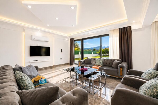 A modern living room with a large flat-screen TV, a glass coffee table, and a sofa set. - Villa Grand Yasar 2 - Four Bedroom Villa, Sleeps 8 (Okçular)