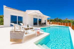 A modern poolside area with lounge chairs, a dining table, and a large pool.