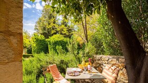 Un espace de restauration en plein air avec une table dressée pour deux personnes, entouré d’une végétation luxuriante et d’un mur de pierre.