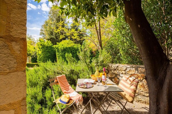 Un espace de restauration en plein air avec une table dressée pour deux personnes, entouré d’une végétation luxuriante et d’un mur de pierre.
