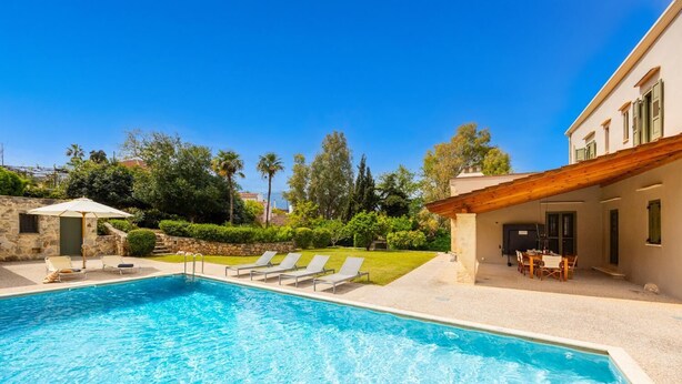 Une piscine avec des chaises longues, un mur en pierre et une pergola en bois.