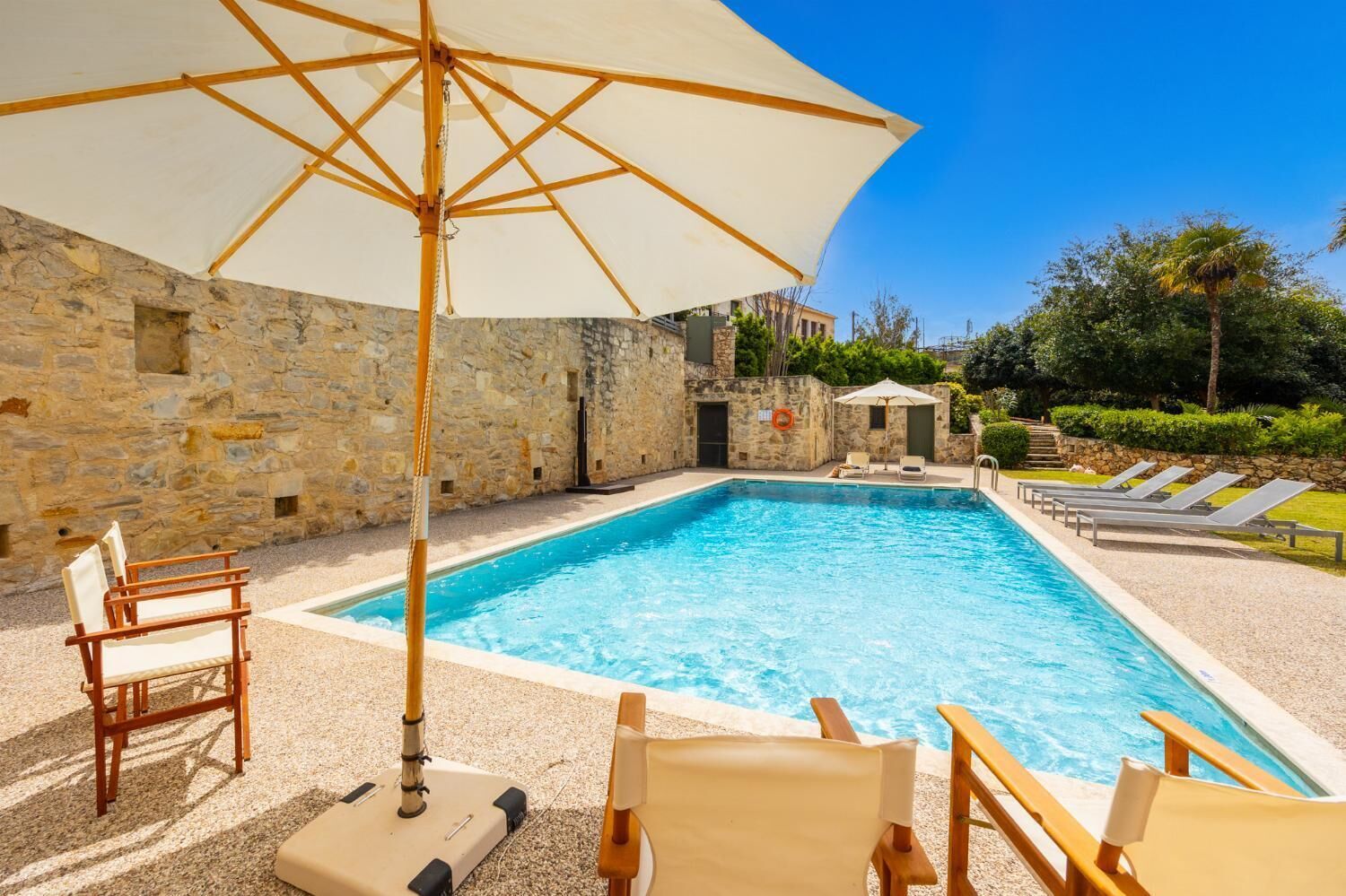 A swimming pool with lounge chairs and umbrellas, surrounded by stone walls and greenery.
