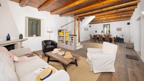 Un vaste espace de vie doté d’un haut plafond en bois, d’une cheminée, d’un fauteuil en cuir noir, d’un canapé blanc et d’un coin repas avec une table et des chaises.