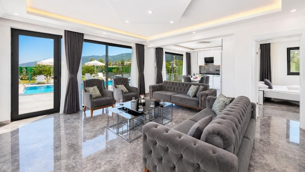 A spacious living room with a large sofa, armchairs, a glass coffee table, and a view of a pool and mountains. - Villa Grand Yasar 1 - Four Bedroom Villa, Sleeps 8 (Okçular)