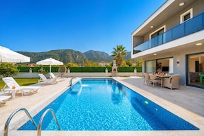 A swimming pool with a view of mountains, outdoor furniture, and a modern building.