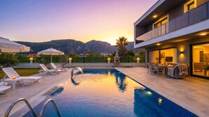A swimming pool with lounge chairs and umbrellas, a patio area with outdoor furniture, and a mountain backdrop. - Villa Grand Yasar 1 - Four Bedroom Villa, Sleeps 8 (Okçular)