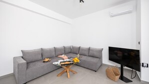 Een moderne woonkamer met een grijze modulaire bank, een glazen salontafel met fruit en een dienblad, een televisie op een meubelstuk en een mand op de vloer.