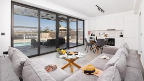 Een moderne woonkamer met een glazen schuindeur die uitkomt op een zwembad, een eethoek en een keuken.