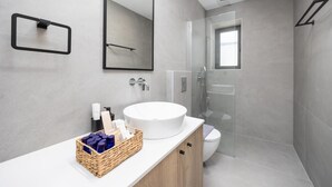 Un baño moderno con un espejo grande, un lavabo blanco y una ducha con mampara de vidrio.
