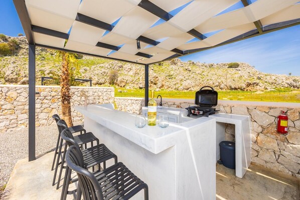 An outdoor bar area with a stone wall, a grill, and a fire extinguisher.