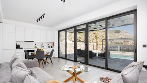 Una sala de estar moderna con una mesa de comedor de vidrio, sofás grises y vistas a una piscina y montañas.