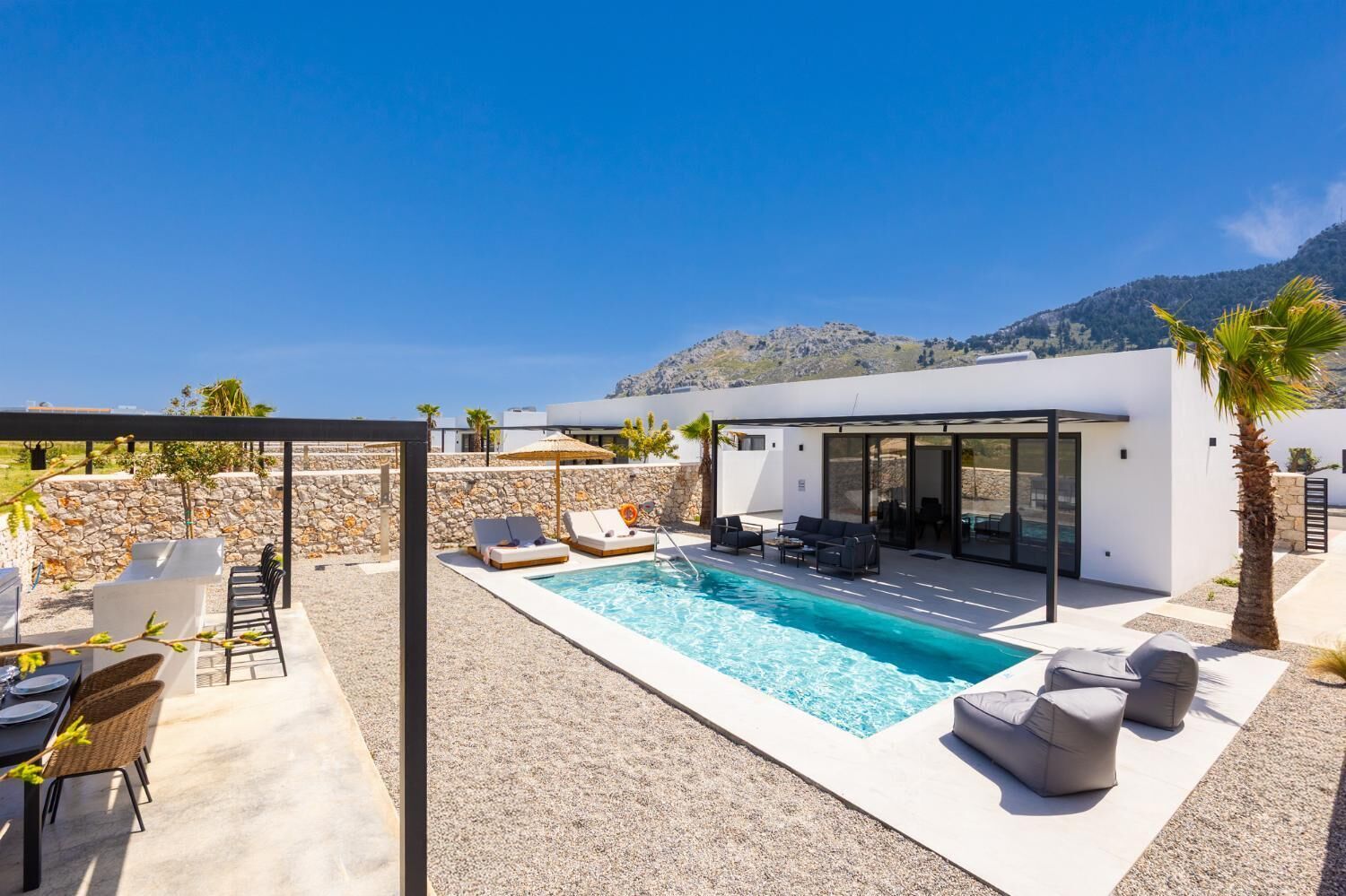 A modern outdoor pool area with lounge chairs, a dining setup, and a glass-enclosed patio.