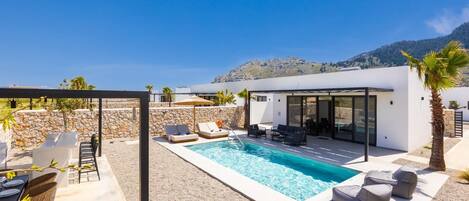 A modern outdoor pool area with lounge chairs, a dining setup, and a glass-enclosed patio.