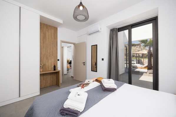 Ein modernes Hotelzimmer mit einem großen Bett, einem Holzschrank, einem Spiegel und Blick ins Freie.