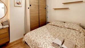 Un dormitorio con cama, armario, mesita de noche, espejo y lámpara colgante.