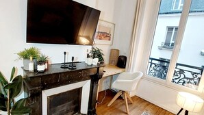 Una sala de estar moderna con chimenea, un televisor de pantalla plana grande montado encima, un escritorio con computadora y vistas al balcón exterior a través de un ventanal amplio.