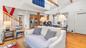 Ein geräumiges Wohnzimmer mit Sofa, Couchtisch und Esstisch mit Stühlen. Im Hintergrund ist eine Küche mit modernen Geräten zu sehen.