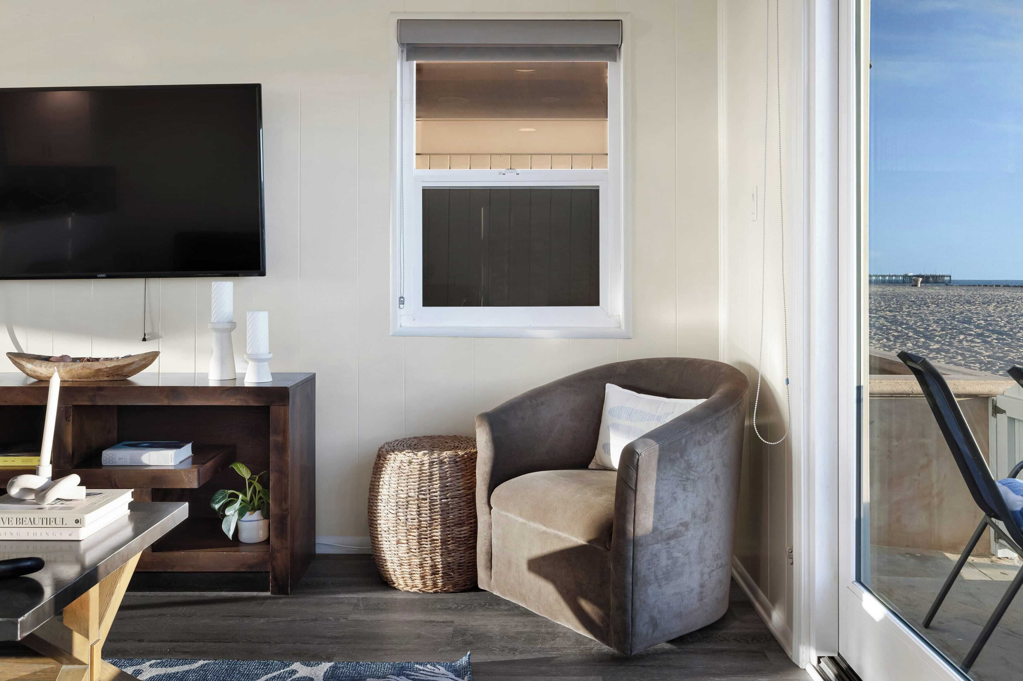 Een woonkamer met een flatscreen televisie, een comfortabele fauteuil, een houten bijzettafeltje en een rieten mand.