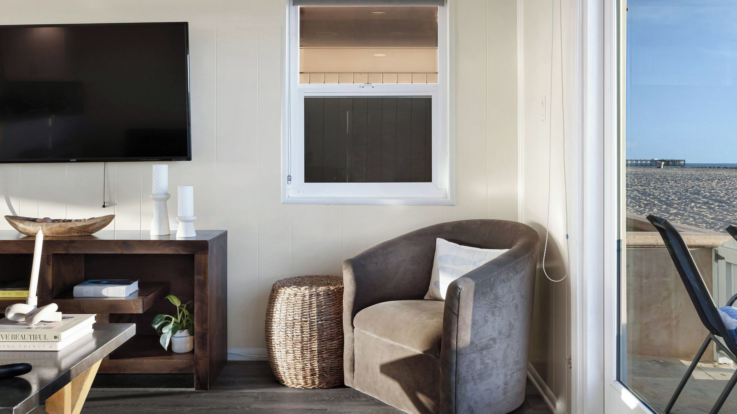 Una sala de estar con televisor, ventana, sillón, mesita de madera y vista a la playa.