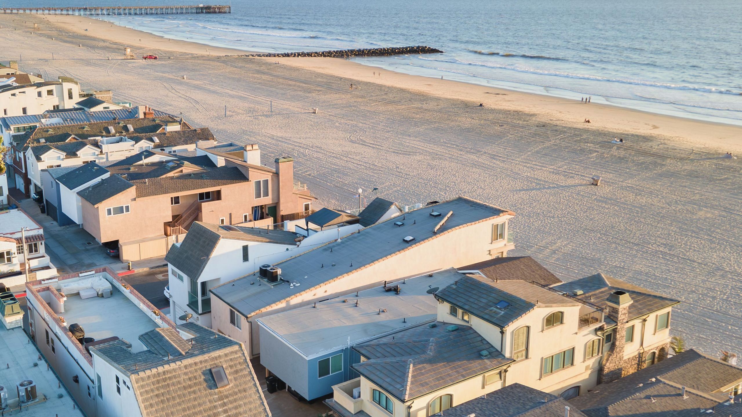 A coastal residential area with houses, a beach, and a pier.