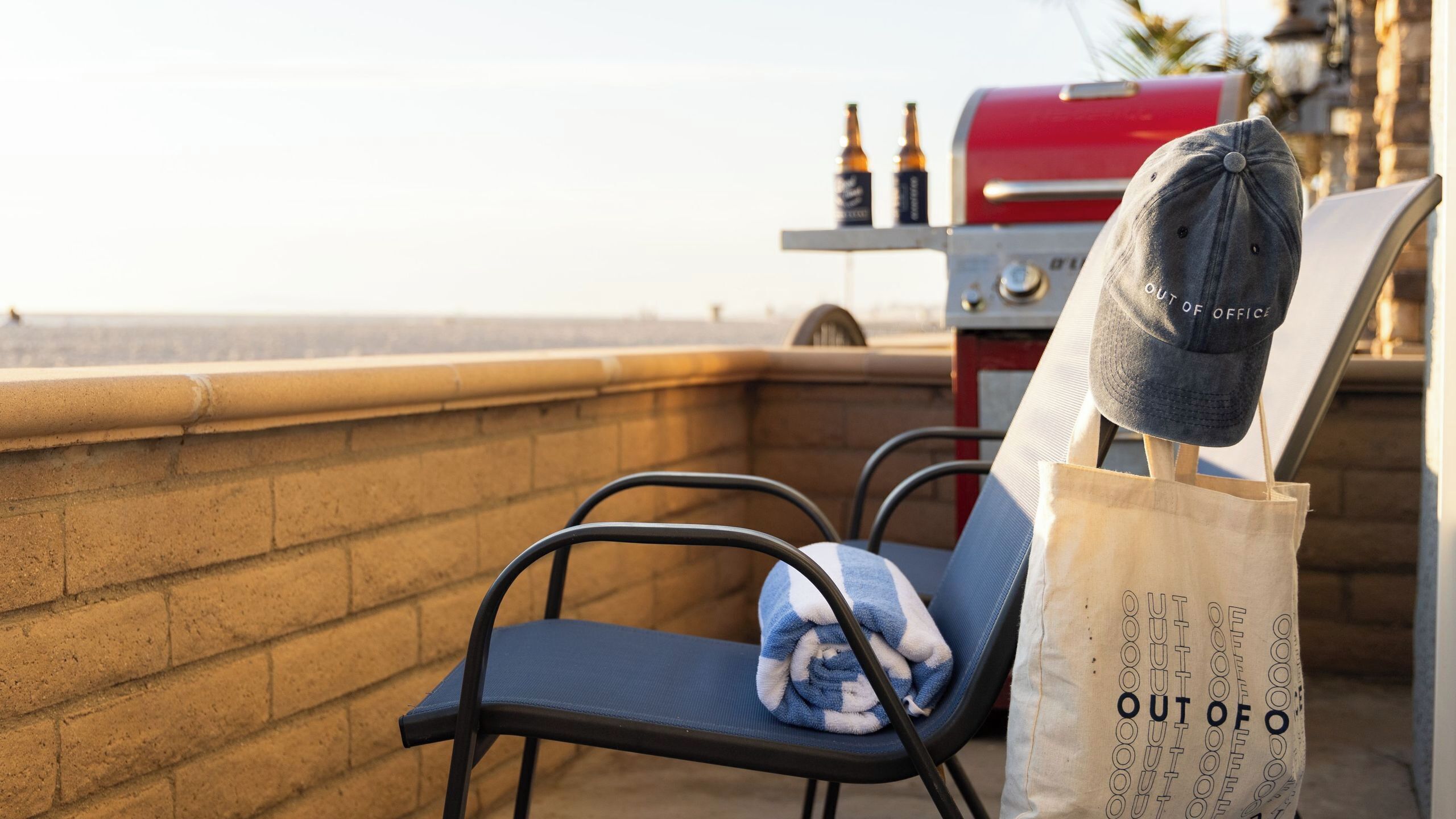 A balcony with a grill, a chair, a towel, and a bag with 'OUT OF OFFICE' text.