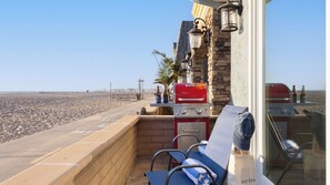 A balcony with a grill, chairs, and a view of the beach.