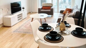 A modern living room with a dining area, a flat-screen TV, and a large window offering a city view. - London Apartment Oasis - Close to City Center (London)