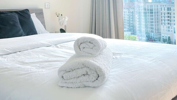 A hotel room with a neatly made bed, a view of city buildings, and a window with curtains. - London Apartment Oasis - Close to City Center (London)