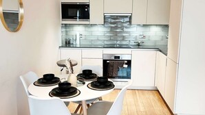 A modern kitchen with white cabinets, a built-in microwave, and a large window. - London Apartment Oasis - Close to City Center (London)