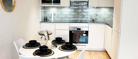 Una cocina moderna con armarios blancos, microondas integrado y un ventanal grande.