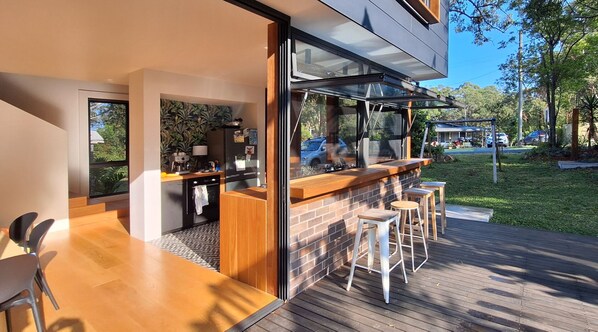 A modern outdoor bar area with a brick counter, wooden stools, and a view of the backyard.