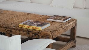 A cozy living room with a white sofa, a wooden coffee table with books, and a wooden bookshelf in the background. - Alapega Live Slow (Alcacer do Sal)