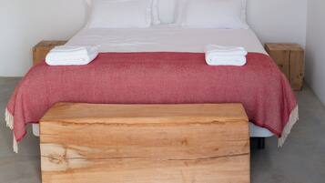 A bed with a wooden bench, white bedding, and a red patterned blanket.