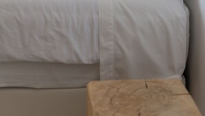 A neatly made bed with white linens and pillows, a wooden bedside table, and a hanging light fixture. - Alapega Live Slow (Alcacer do Sal)
