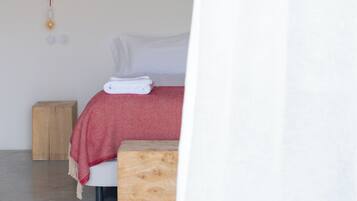 Un dormitorio minimalista con una cama, una mesita de noche de madera y una lámpara colgante.
