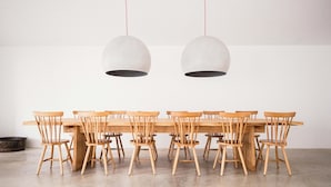 A dining area with a long wooden table and matching chairs, two hanging pendant lights, and a concrete floor. - Alapega Live Slow (Alcacer do Sal)