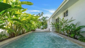 Une piscine entourée de chaises longues et bordée d’une végétation tropicale luxuriante.