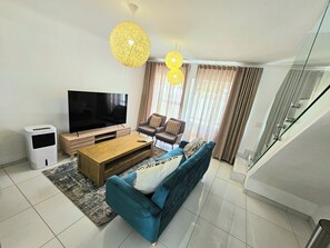 Een moderne woonkamer met een flatscreen televisie, een houten salontafel, een blauwe bank en een glazen trap.