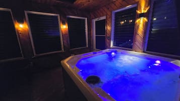 A hot tub with blue lighting inside a wooden cabin with windows.