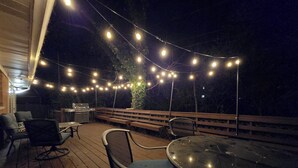 An outdoor deck with string lights, wooden benches, and a grill.