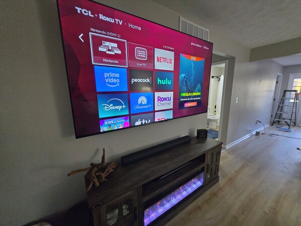 Un televisor TCL Roku montado en una pared con un mueble de entretenimiento de madera debajo.