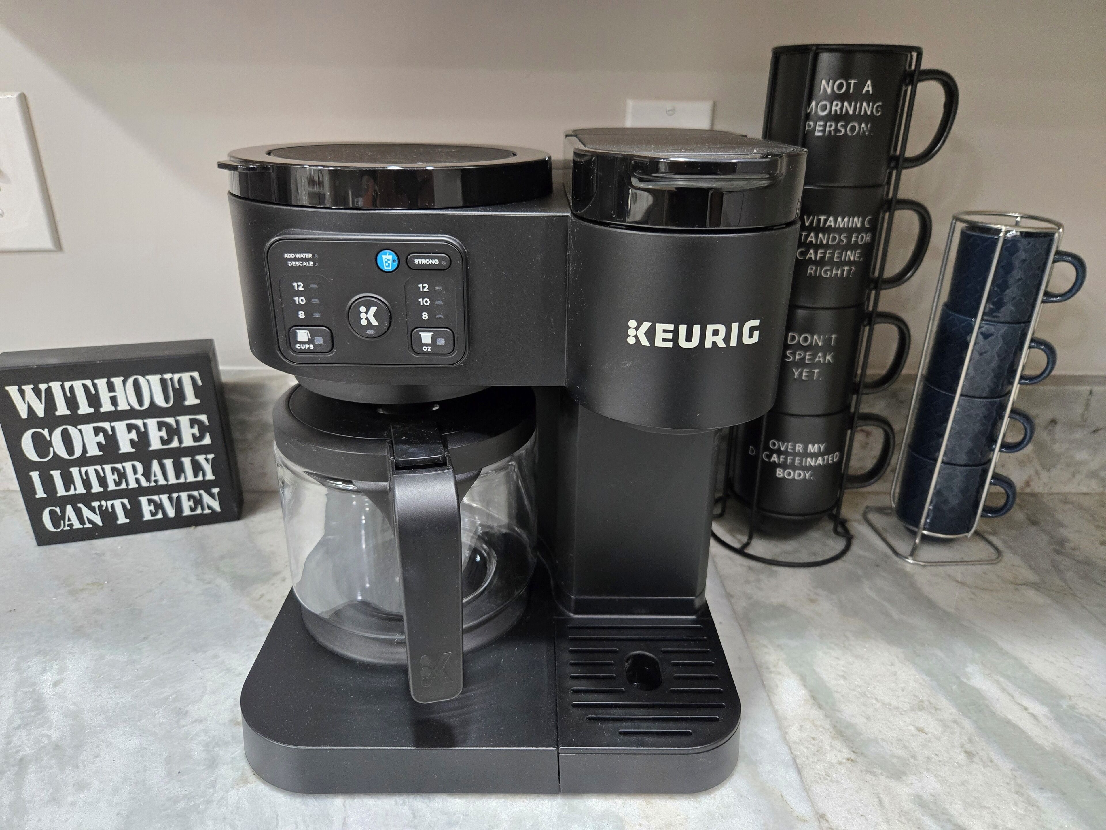 A Keurig coffee maker on a kitchen counter with a sign that reads "WITHOUT COFFEE I LITERALLY CAN'T EVEN".