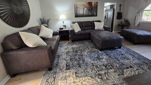 A modern living room with a sectional sofa, a patterned rug, and a painting on the wall.