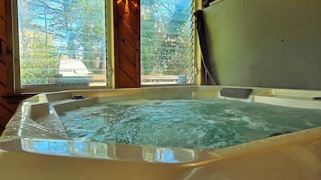A hot tub with a wooden interior and a view of trees through a window.