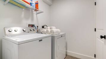 A laundry area with a front-loading washer and dryer, a shelf with laundry supplies, and a door to the right.