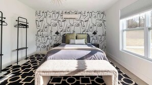 A bedroom with a patterned wall, a bed with a geometric rug, a window, and a modern light fixture. - Gallery House: Designer Home-Hot Tub-Campfire-EV (Ithaca)