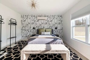 Ett sovrum med en vägg som har ett mönster, en säng med en geometrisk matta, ett fönster och en modern lampa.