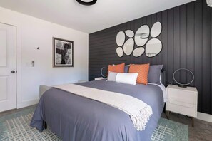 A modern bedroom with a large bed, a bedside table, a wall-mounted mirror, and a framed picture. - Gallery House: Designer Home-Hot Tub-Campfire-EV (Ithaca)