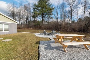 A backyard with a picnic table and chairs, a small patio area, and a building in the background.